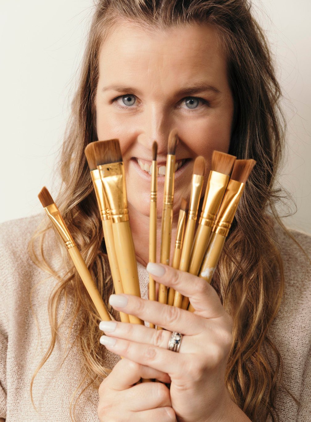 Bec holding a bunch of paintbrushes in front of her face
